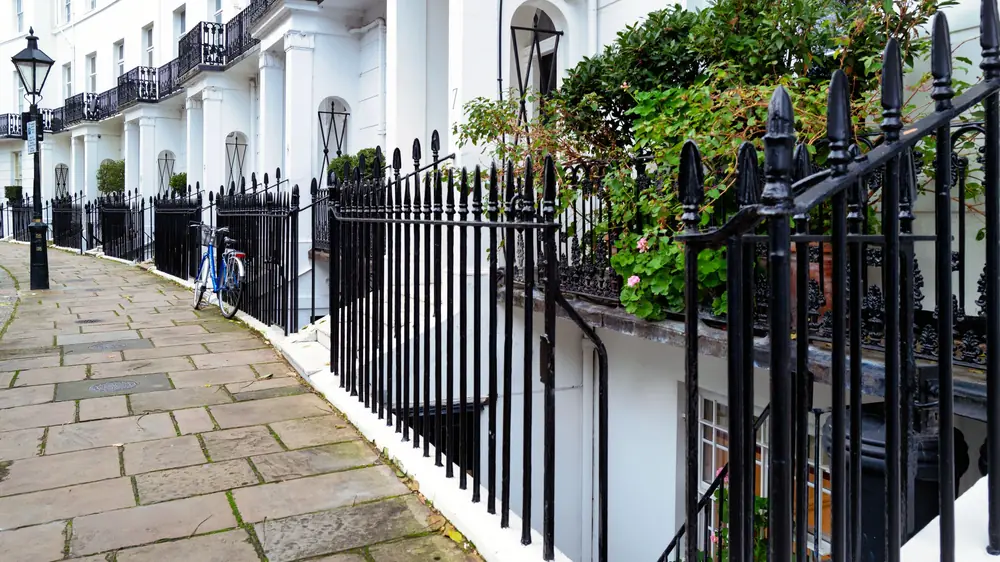 White stucco Kensington terrace beyond black cast-iron area railings and a lightwell above a flagstone pavement