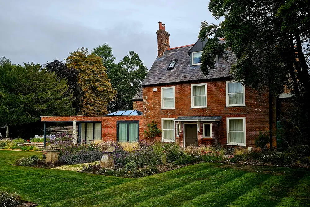 Period house in red brick with a low glass garden-room extension, a striped lawn and planted borders in front