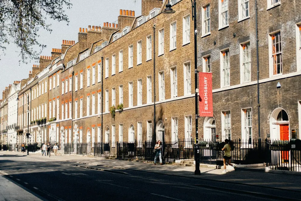 Unbroken row of Georgian brick townhouses in Bloomsbury, with chimney stacks, fanlights over the doors and black iron railings