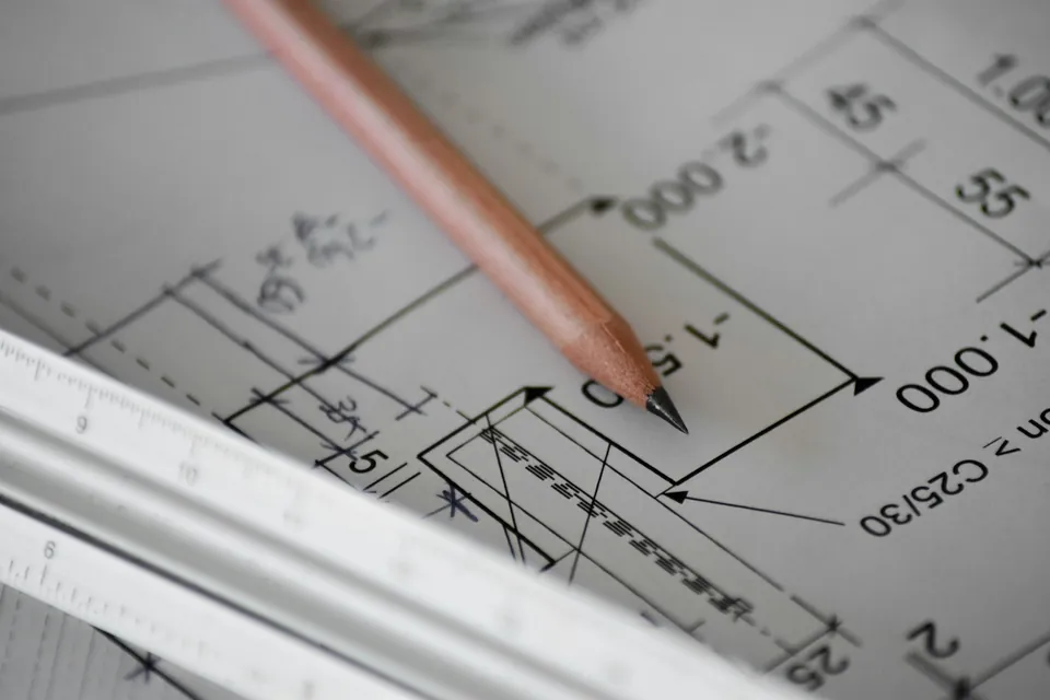 Pencil resting on a dimensioned technical drawing beside a scale rule