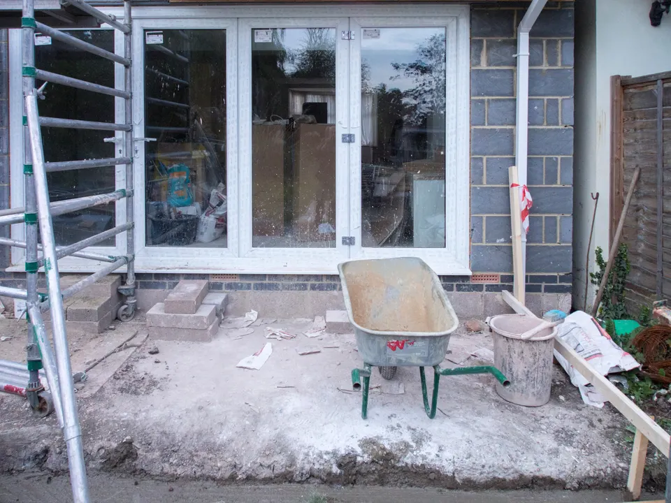 House extension under construction with scaffolding, new glazed doors and building materials